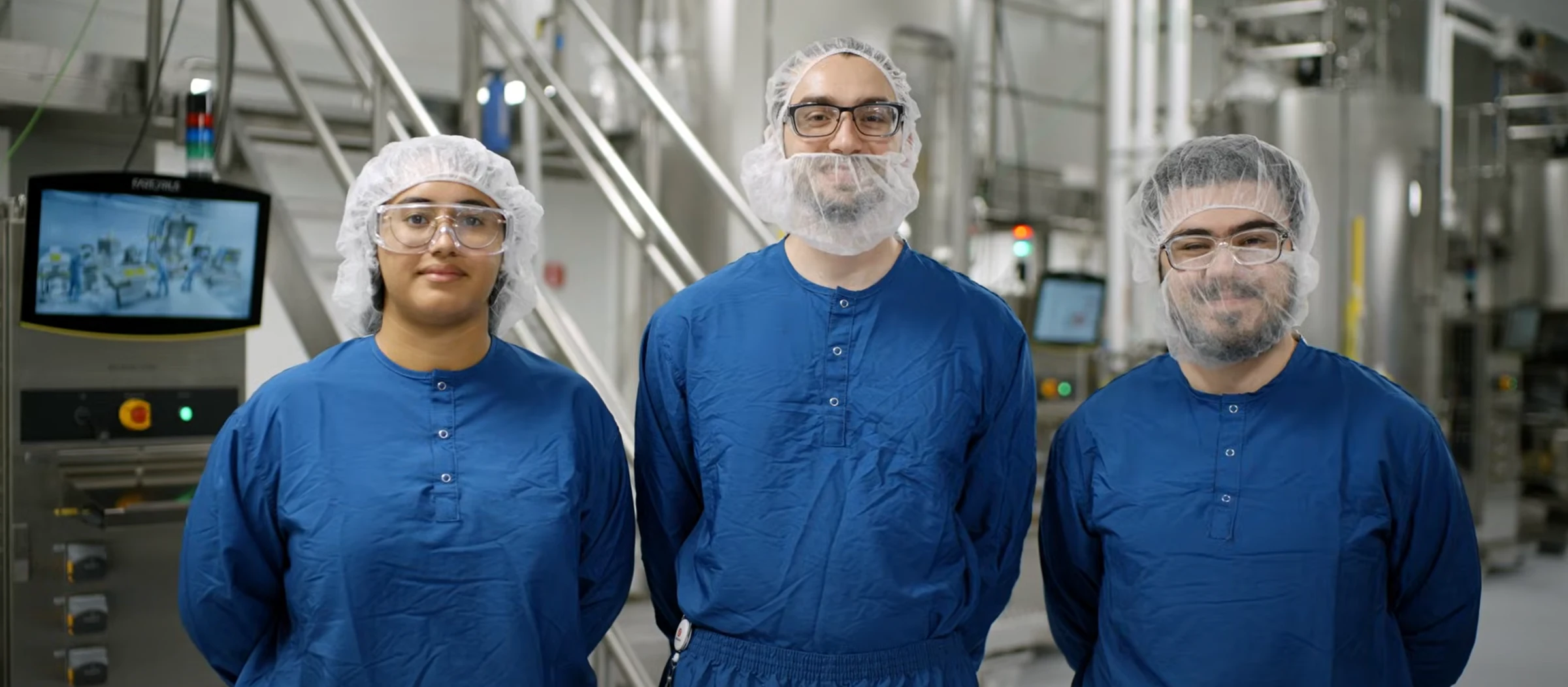 Workers in blue uniforms and hairnets smiling in a factory. Join the team with BeOne Careers.